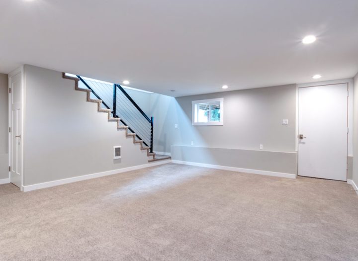 An empty remodeled basement of a house with carpeted floor, newly painted walls and ceilings, and recessed lights