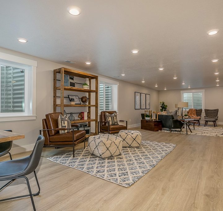 Basement area remodeled for lounging; it has laminate flooring, a decorative carpet, and different sets of chairs and tables