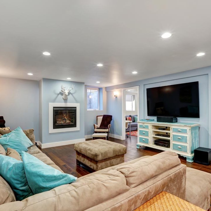 A basement area for entertainment room, a huge couch, blue and white painted TV cabinet, a wide flat screen, and a fireplace on one side