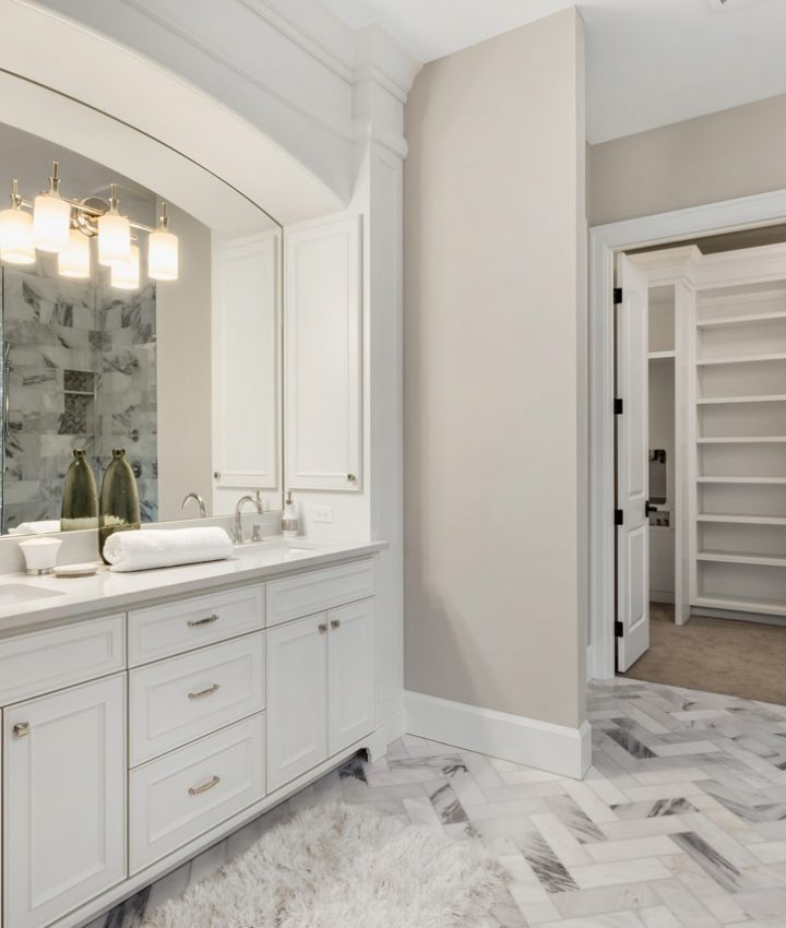 A bathroom with access to the walk-in closet, floor tiles of herringbone design, and white vanity cabinets