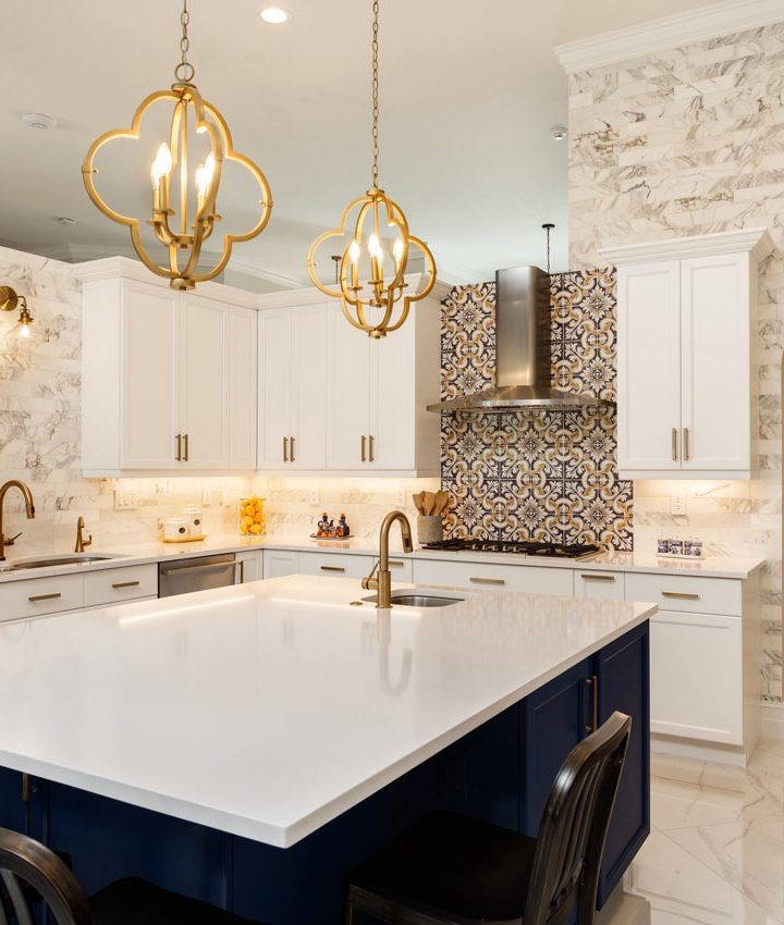 A contemporary kitchen with island, and a patterned backsplash, with white cabinets and artistic pendant lights